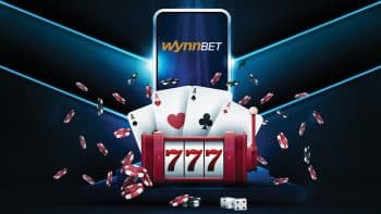 reel slot featuring the 777 combination and a cards hand in front of a phone featuring the wynnbetlogo with chips floating mid air on a dark blue background